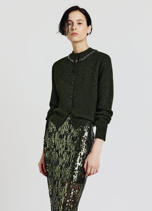 Dunkelgrüner Cardigan mit perlenbesetztem Kragen, ausgestattet mit einer Knopfverschluss und gerippten Bündchen. Kombiniert mit einem schwarzen Paillettenrock.