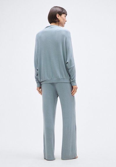 Világoskék, hosszú ujjú felső és hozzá illő, bő szárú nadrág puha, sima anyagból. Laza szabás, minimalista dizájn minták vagy díszítések nélkül.