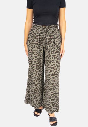 Frau trägt hochtaillierte, weit geschnittene Hose mit Leopardenmuster, Kordelzug an der Taille, schwarzes, kurzärmeliges, enganliegendes Oberteil und schwarze Sandalen.