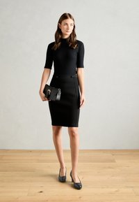 Černý přiléhavý top s krátkými rukávy, spárovaný s černou pouzdrovou sukní po kolena s knoflíkovými detaily a černými vysokými podpatky.