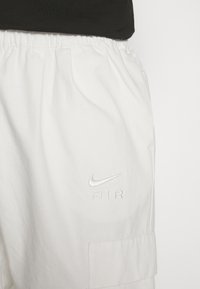 White Nike shorts feature an elastic waistband and an embroidered "Nike AIR" logo. Includes a side pocket with a flap. Smooth cotton texture.