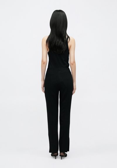 Fekete ujjatlan felső hozzáillő, testhezálló fekete nadrággal. A nadrág egyenes szabású, enyhe hasítékokkal a szárvégeken. Simaságot és matt textúrát mutat.