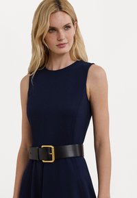Vestido sem mangas azul-marinho com um corpete justo, apresentando um cinto largo de couro preto com uma fivela dourada que acentua a cintura.