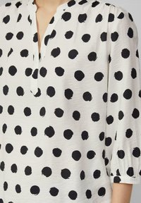 Witte blouse met grote zwarte stippen. De materialen lijken lichtgewicht met een gestructureerde afwerking. V-halslijn en geraffineerde mouwen.