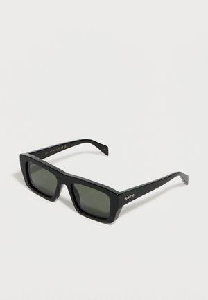 Lunettes de soleil Gucci rectangulaires noires avec montures épaisses et verres foncés, présentées sur un fond blanc.