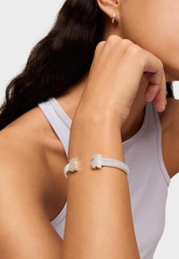 Pulsera de plata con diseño de malla, con acentos en forma de oso. Se ajusta alrededor de la muñeca, mostrando una textura suave y un acabado brillante.