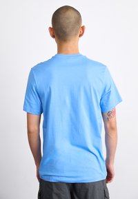 Svjetloplavi pamučni majica s kružnim izrezom i kratkim rukavima, glatke teksture i opuštenog kroja. Bez vidljivih grafika ili uzoraka.