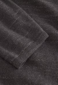 Tessuto a maglia grigio scuro con una consistenza morbida, caratterizzato da leggere variazioni di colore e un bordo pulito sulla manica ripiegata.
