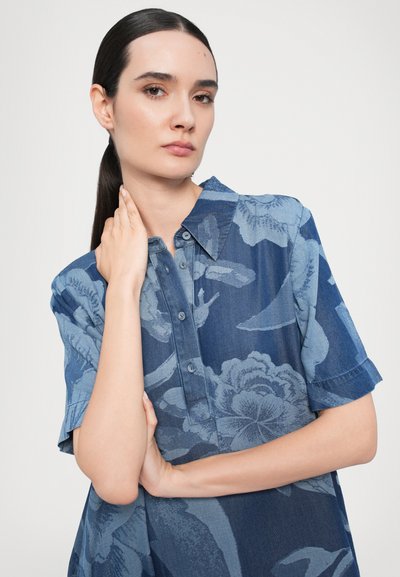 Cămașă cu model floral albastru, cu mâneci scurte, închidere cu nasturi și guler. Fabricată dintr-un material ușor, cu nuanțe variate de albastru.