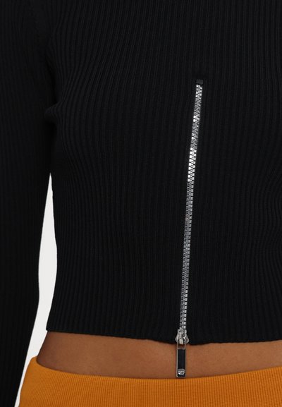 Fekete bordázott crop top, középen fényes ezüst cipzárral. Az alja narancssárga sávba ér, kiemelve a kontrasztos színeket.