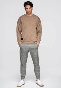 Beige teksturoitu collegepaita, jossa on hienovarainen kuvio, yhdistetty harmaisiin ruutukuosisiin kapea lahkeisiin housuihin ja valkoisiin lenkkareihin, joissa on beigejä yksityiskohtia.