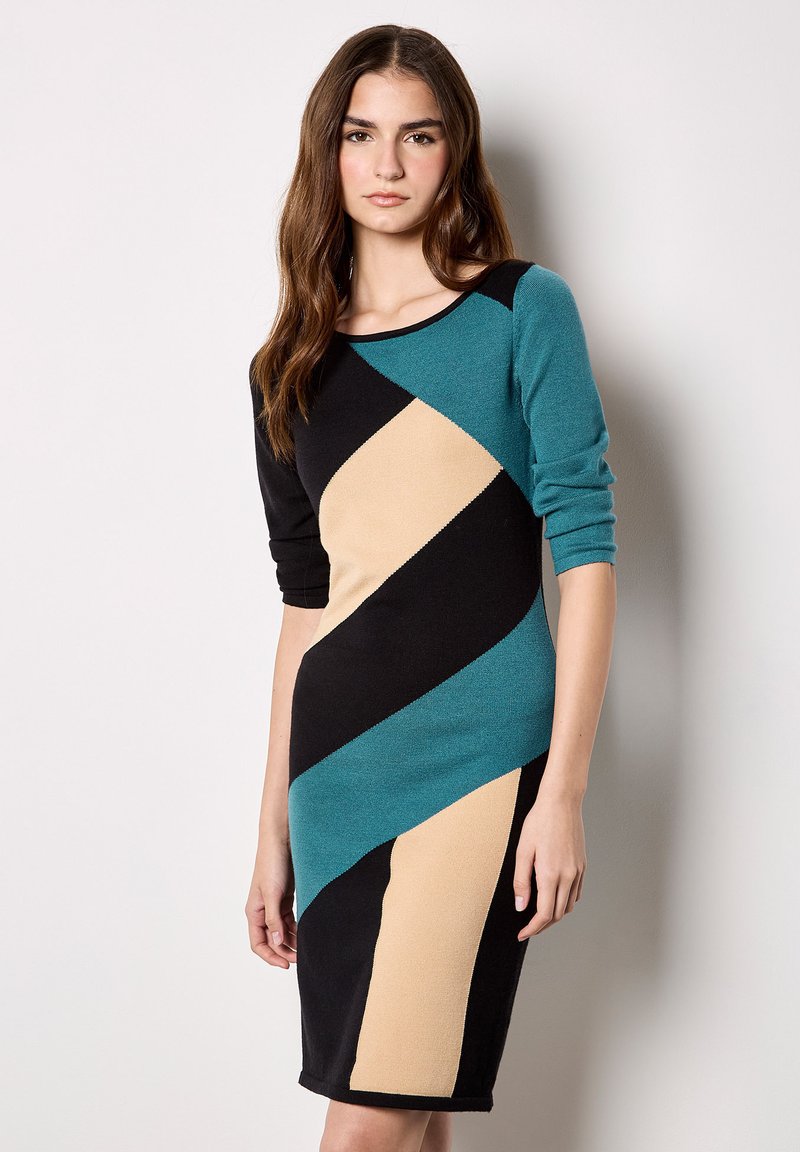 Strickkleid in Türkis, Schwarz und Beige mit diagonalen Farbkombinationen; hat dreiviertel Ärmel und einen runden Ausschnitt.