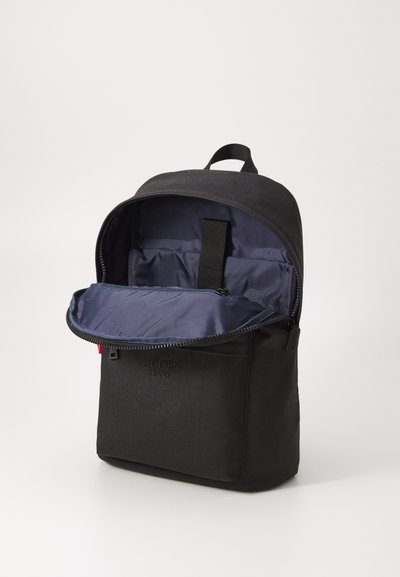 Sac à dos noir au toucher lisse, avec une ouverture zippée et un intérieur bleu marine. Logo embossé sur la poche avant. Design compact.