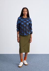 Maglione a maglia floreale blu e nero, gonna midi verde oliva, calzettoni arancioni e sneakers bianche. Vestibilità rilassata, scollatura rotonda, texture morbida.