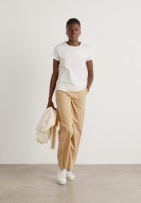 White short-sleeve t-shirt paired with beige wide-leg trousers and white sneakers. A cream-colored blazer is draped over the left arm.