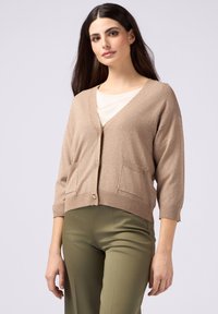 Beige, texturerad kofta med V-hals, trekvartsärmar och två framfickor, med knäppning och diskret glans.