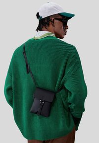 Grønne ribbede trøje med oversized pasform, parret med en lille sort crossbody taske med klap og justerbar rem. Hvid kasket.