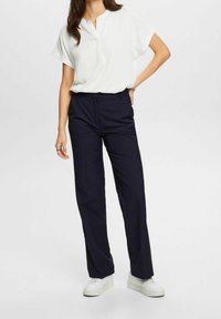Bílé krátké rukávy blouse s polořadovým zapínáním, kombinované s tmavě námořnickými rovnými kalhotami a bílými platformovými teniskami.