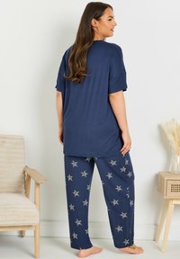 Nattlinneset i marinblått som har en löst sittande t-shirt och byxor med stjärnmönster. Tyget verkar mjukt och har en avslappnad design.