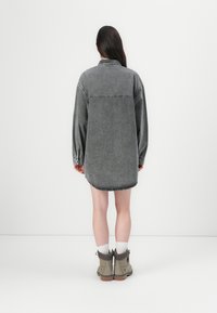 Denim skjortekjole i grå, med lange ermer, knappestolpe og buet hem. Brukt med beige ankelstøvler og hvite sokker.