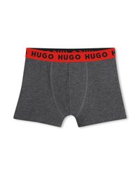 Σκούρα γκρι ανδρικά εσώρουχα boxer με κόκκινη ζώνη μέσης που φέρει επαναλαμβανόμενο μαύρο κείμενο "HUGO", απλωμένα επίπεδα σε λευκό φόντο.