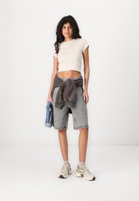 Beige cropped t-shirt, gray sweatshirt tied at the waist, light gray denim shorts, and beige athletic shoes with darker accents.