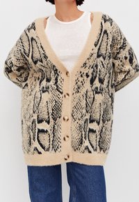 Beige Oversized-Cardigan mit einem schwarzen Schlangenprint-Muster, V-Ausschnitt, kurzen Ärmeln und fünf Knöpfen vorne. Weicher, strukturierter Stoff.
