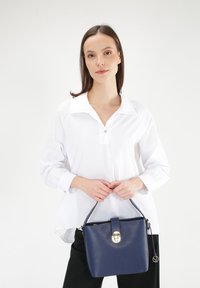 Navy blue leather handbag with a textured finish, a top handle, gold hardware, and a zip closure with a decorative clasp.