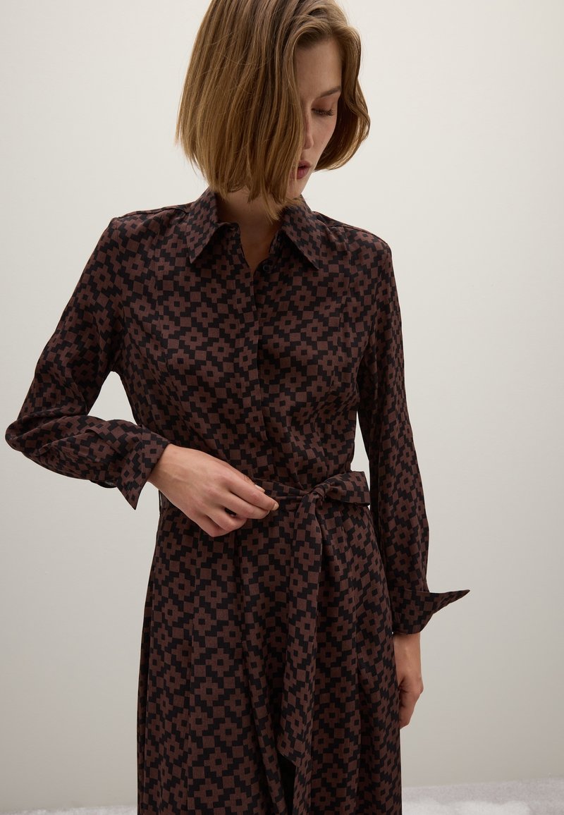 Braun gemustertes Hemdkleid mit langen Ärmeln, Kragen und Gürtel in der Taille. Das Material wirkt glatt und hat ein geometrisches Design in dunkleren Tönen.