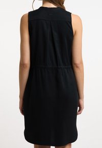 Vestido negro sin mangas con cintura elástica, textura suave, cuello redondo y detalle de pliegue en la parte posterior.