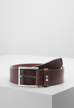 Brązowy skórzany pasek z prostokątną srebrną klamrą i małym metalowym logo, zwinięty na białej powierzchni.