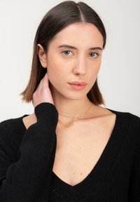 Maglione nero a maglia con scollatura a V profonda e texture a coste. Il modello ha i capelli fino alle spalle, una delicata collana d'argento e trucco neutro.