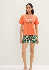 Oranges Baumwoll-T-Shirt mit dem Text "LOVE IS LOVE", kombiniert mit grünen Shorts, die ein pinkes und beige Blattmuster aufweisen. Weicher Stoff und lässige Passform.