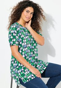 Multikleurige T-shirt met korte mouwen en geometrische patronen in groen, blauw en wit. Lichte stof, ontspannen pasvorm en afgeronde zoom.