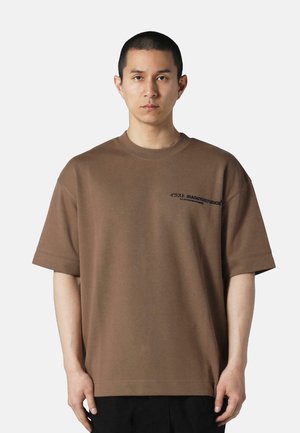 Braunes, übergroßes T-Shirt aus glattem Stoff. Mit kurzen Ärmeln und einem Logo-Design auf der linken Brustseite.