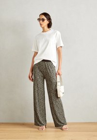 Hvit t-skjorte med Marc O'Polo-logo, svart-hvite mønstrede vide bukser, klare solbriller, og en hvit crossover-veske.