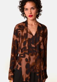 Bruine en zwarte blouse met patroon, met een wikkeldesign, lange mouwen en een zachte, zijden textuur. Heeft een V-halslijn en een striktaille.