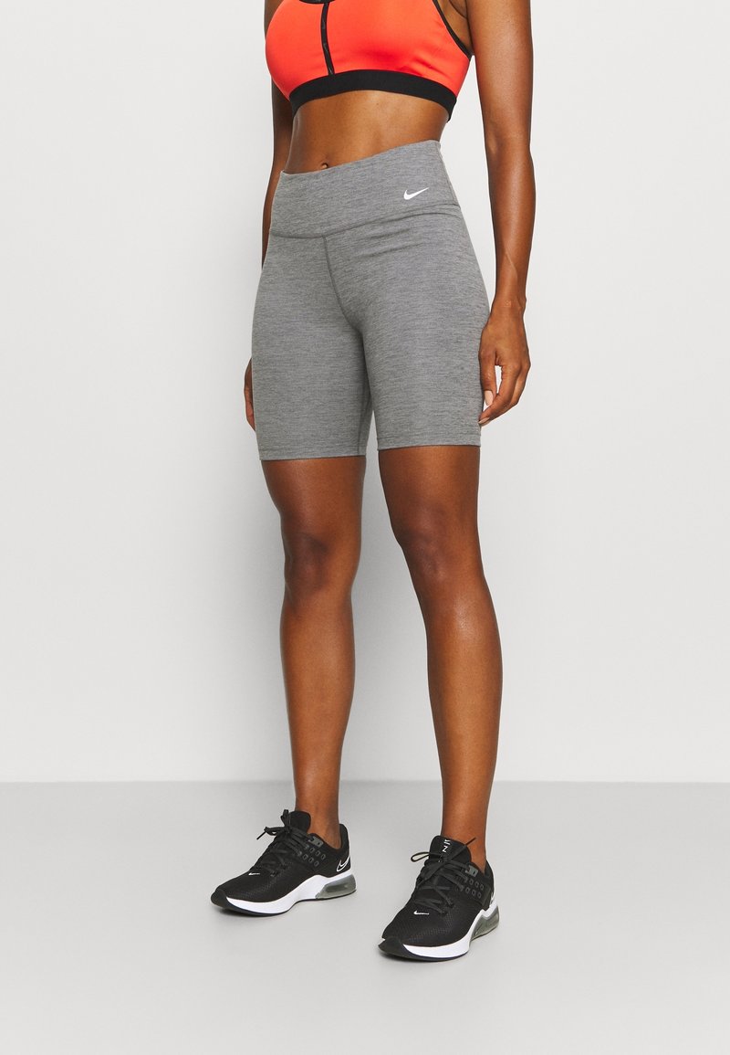 Shorts de sport gris avec une taille haute, associés à un soutien-gorge de sport noir et orange. Des baskets noires avec des accents blancs complètent le look.