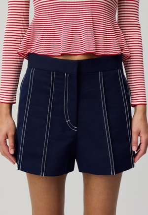 Pantaloni corti in cotone blu navy con dettagli in cucitura bianca, dotati di una parte anteriore piatta e una vita liscia. Adatti per un abbigliamento casual.