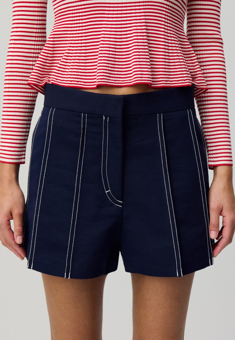 Pantaloni corti in cotone blu navy con dettagli in cucitura bianca, dotati di una parte anteriore piatta e una vita liscia. Adatti per un abbigliamento casual.