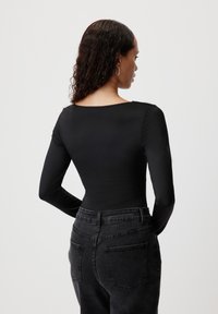 Černý bodysuit s dlouhým rukávem, hladkého materiálu a širokým výstřihem, v kombinaci s tmavými džínami s vysokým pasem a jemně vystouplými zadními kapsami.