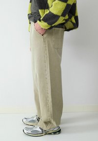 Beige wijde jeans van een katoenmix, met een achterzak. Gecombineerd met metallic sneakers. Getextureerde groene en zwarte geblokte jas zichtbaar.