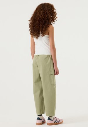 Pantalon cargo en coton vert à coupe ample, avec poches latérales et ourlets retroussés, associé à des baskets multicolores et un haut blanc uni.