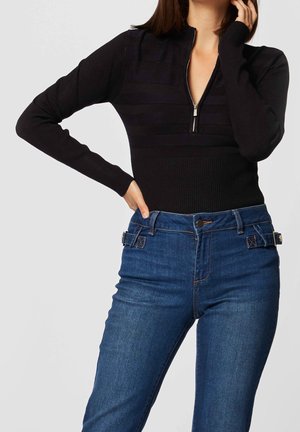 Mustat vetoketjulliset yläosat, joissa on ribbed-tekstuuri ja raidallinen kuvio; yhdistetty korkea vyötäröiset siniset farkut, joissa on sivuklipsit.