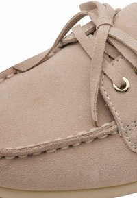 Chaussure en daim rose clair avec un bout arrondi, des œillets dorés et un lacet assorti. Présente une couture visible et une texture douce.