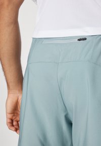 Pantalones cortos azul claro con una textura suave, que cuentan con un bolsillo con cremallera en la parte trasera y un corte clásico. Están dispuestos de forma plana, con mínimas costuras visibles.