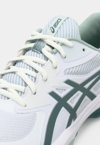 White athletic shoe with mesh material and green accents. Features white laces, textured overlays, and a prominent logo on the tongue.