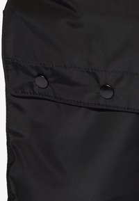 Černá nylonová tkanina s hladkou texturou, se dvěma černými patentkami a jednoduchým designem, vhodná pro svrchní oděvy nebo doplňky.