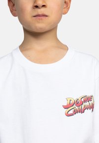 Bílé bavlněné tričko s barevným logem "DC Shoe Company" na levé straně hrudi. Kulatý výstřih a krátké rukávy. Hladká textura.