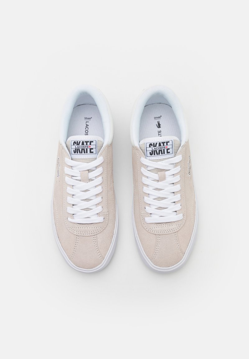 Baskets en daim beige avec semelle en caoutchouc blanche. Comprend des lacets blancs, un col rembourré et une languette de marque étiquetée "SKATE LACOSTE."